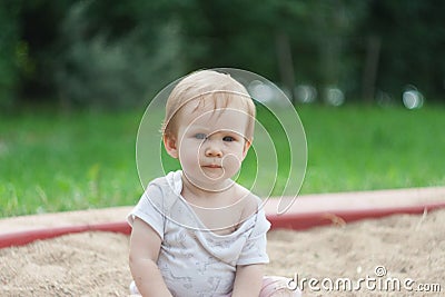 A little quiet girl sits in a sandbox on the sand Stock Photo