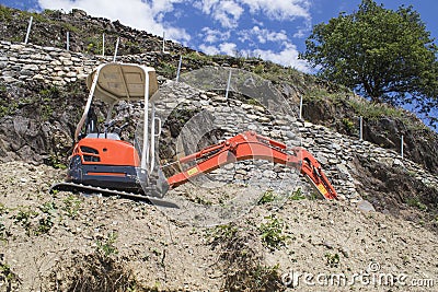 Little red excavator on a mountain with trees Stock Photo