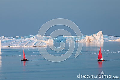 Little red sailboat cruising among floating icebergs in Disko Bay glacier during midnight sun season of polar summer. Greenland Stock Photo