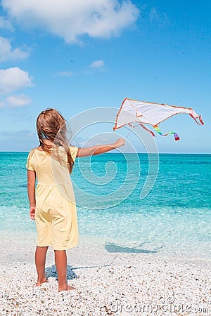 Little running girl with flying kite on tropical beach. Kid play on ocean shore. Stock Photo