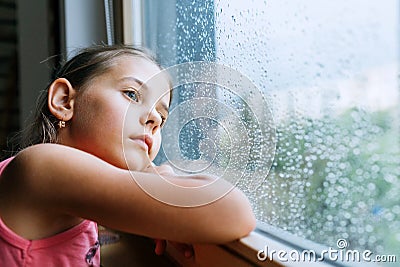 Little sad girl pensive looking through the window glass with a lot of raindrops. Sadness childhood concept image Stock Photo