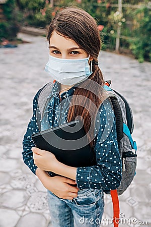 Little schoolgirl with a medical mask on her face and a laptop in her hand goes to school Stock Photo