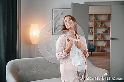 Little shirt for a baby. Beautiful pregnant woman is indoors at home Stock Photo