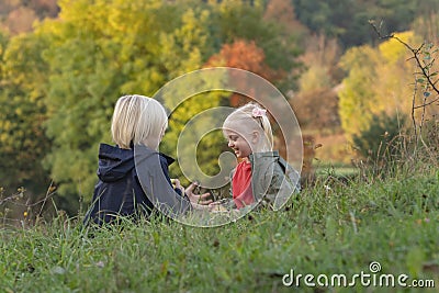 Little siblings resting in nature. Blond boy and girl sit on grass and eat apples. Children on picnic on autumn day Stock Photo