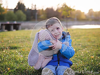 Little Slavic joyful boy on the lawn portrait in the spring in a city park with a soft toy Stock Photo