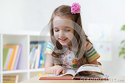 Little smart girl looking at book while sitting on chair in nursery Stock Photo