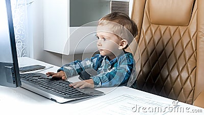 Little smart toddler boy sitting in office and working on computer Stock Photo