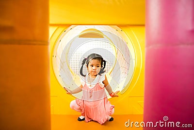 A little smile girl is crawling out of yellow tunnel at playground Stock Photo