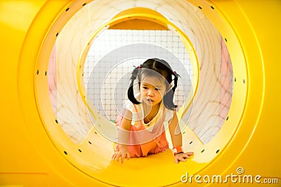 A little smile girl is crawling out of yellow tunnel at playground Stock Photo