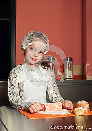 Little smiling girl dressed as a baker prepares buns in the kitchen Stock Photo