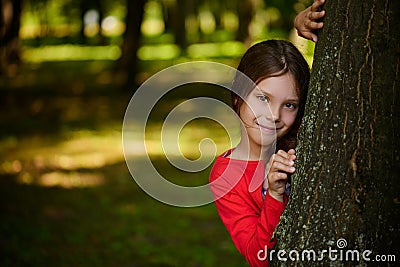 Little smiling girl is hiding behind tree Stock Photo