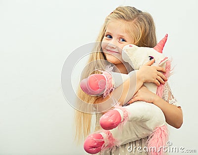 Little smiling girl with white unicorn toy. Stock Photo