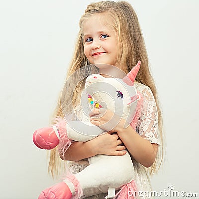 Little smiling girl with white unicorn toy. Stock Photo