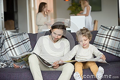 Little son pretending reading newspaper sitting on couch with fa Stock Photo