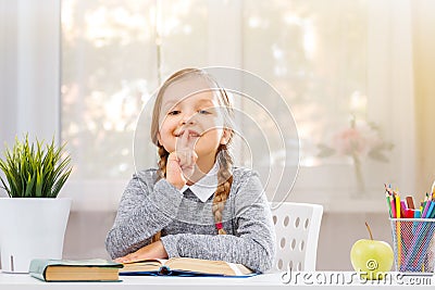 Little student girl sitting at the table and reading a book. The child shows a sign shh. The concept of education and school. Stock Photo