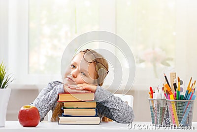 Little student girl sitting at the table. Tired schoolgirl with a pile of books. Education. Back to school. In the background is Stock Photo