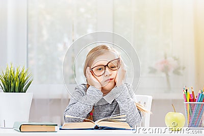 Little student girl sitting at the table. Tired schoolgirl with a pile of books. Education. Back to school. Stock Photo