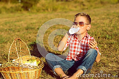 Little stylish boy in sunglasses is drinking yogurt on the meadow Stock Photo