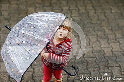 Little toddler girl playing with big umbrella on rainy day. Happy positive child running through rain, puddles Stock Photo