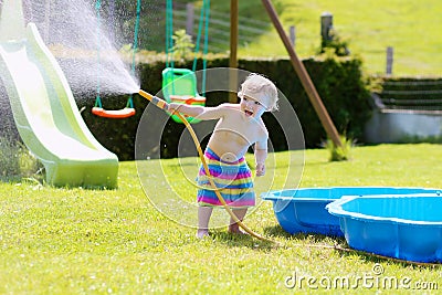 Little toddler girl playing with water hose in the garden Stock Photo