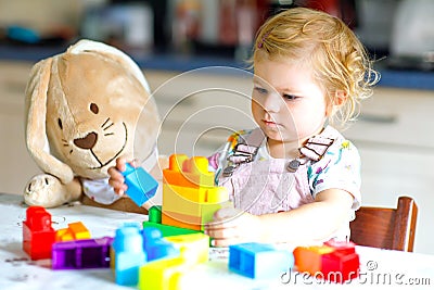 Little toddler girl with plush bunny playing with educational plastic colorful blocs toys. child having fun. Creative Stock Photo