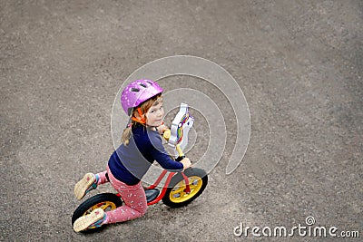 Little toddler girl running with balance bike on summer day. Happy child driving, biking with bicycle, outdoor activity Stock Photo