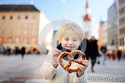 Little tourist holding traditional bavarian bread called pretzel on the town hall building background in Munich, Germany Stock Photo