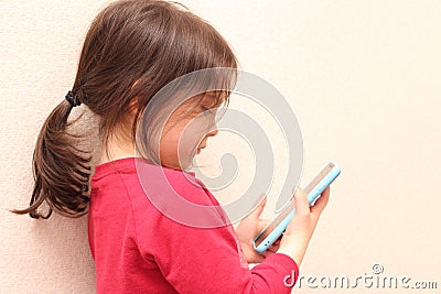 A little white girl with a ponytail takes a picture of her sister on a cell phone against the background of a regular apartment Stock Photo