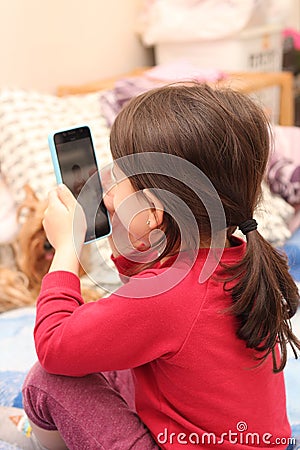 A little white girl with a ponytail takes a picture of her sister on a cell phone against the background of a regular apartment Stock Photo