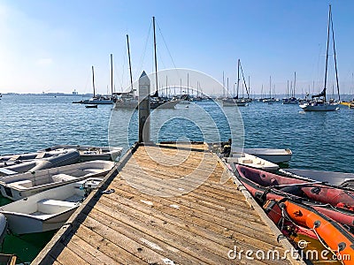 Little wood pier with small abandoned boat and Sailing boat on the background during blue sky day Editorial Stock Photo