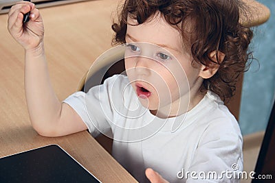 Little 2 3 year old baby girl in white clothers draws at the home computer in graphics drawing tablet. The child is holding a pen Stock Photo