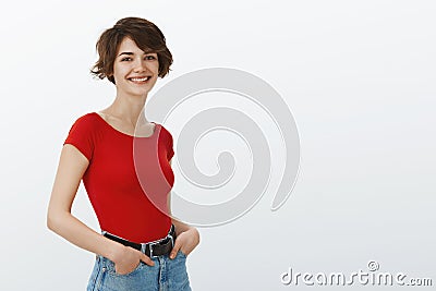 Lively attractive self-assured female trendy red t-shirt hold hands pockets stand profile turn camera smiling amused Stock Photo