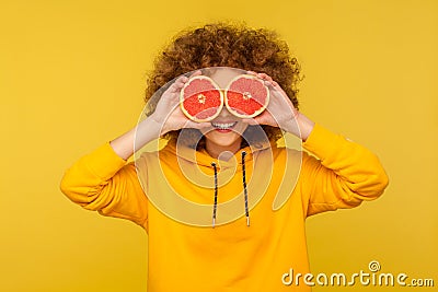 Lively vivid energetic woman with fluffy curly hairstyle covering eyes with half slice grapefruit, detox Stock Photo