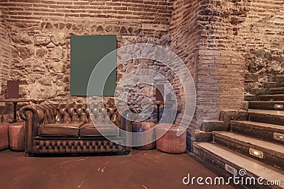 Living room of a nightlife venue with a shiny brown leather chester sofa, exposed stone and brick walls and stairs with indicative Editorial Stock Photo