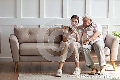 On one side of sofa sitting grandfather with adult granddaughter Stock Photo