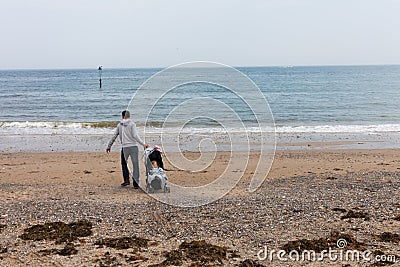 LLandudno, Wales, UK - MAY 27, 2018 Father with baby in baby carriage walking on the beach. Single parent with baby on the seashor Editorial Stock Photo