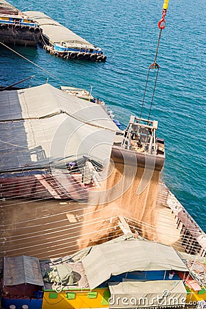 Loading wheat on cargo ship with crane and bucket. Shipment from a merchant ship to a small ship. Grapple crane fill wheat into Stock Photo