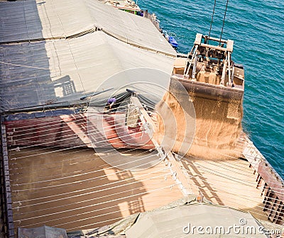 Loading wheat on cargo ship with crane and bucket. Shipment from a merchant ship to a small ship. Grapple crane fill wheat into Stock Photo