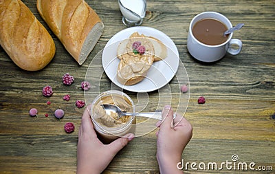 A loaf of bread and a sandwich a piece of loaf with nut paste a Cup and children`s hands holding a jar with nut paste and berry Stock Photo