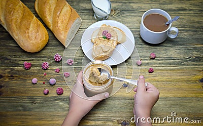 A loaf of bread and a sandwich a piece of loaf with nut paste a Cup and children`s hands holding a jar with nut paste and berry Stock Photo