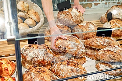 Loaves of bread at a bakery counter being sold and picked by a baker, behind a pane of glass. European artisan bread store, retail Stock Photo