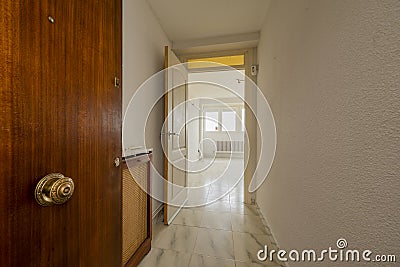 Lobby of a house with a solid wooden access door, a small corridor, white veined tiled floors and a radiator cover with grilles Stock Photo