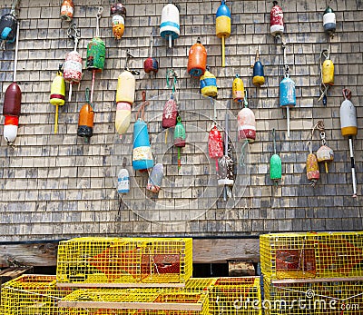 Lobster buoys hanging on the wall of a building with yellow lobster pots on the ground Stock Photo