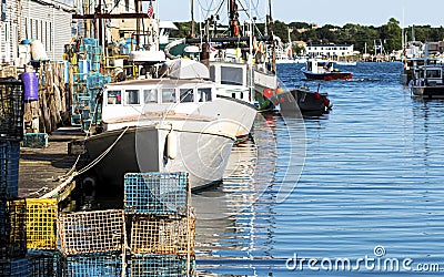 Lobster fishing boats docked in a canal with lobster traps pilled on the dock in Portland Maine Editorial Stock Photo