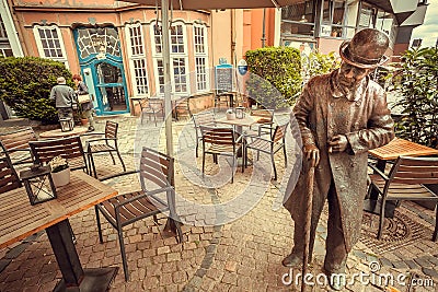 Local cafe, restaurants and sculpture of walking pedestrian on narrow street of old town Editorial Stock Photo