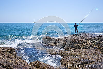 A local fisher man with his fishing rod is looking the boat in the ocean on rocks sea coast, shore of the Bay in Asia, Thailand Editorial Stock Photo