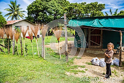 Local native indigenous Polynesian girl sells hand made brooms and plastic bags with sweet potato kumara, Tonga. A poor hut. Editorial Stock Photo