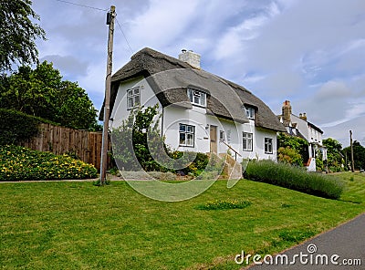 View of a traditional English cottage and thatched roof with a well painted lawn area. Editorial Stock Photo