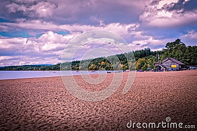 Loch Morlich sandy gravel shore, Aviemore, near the boathouse cafe on a cloudy day with green trees in the background Stock Photo