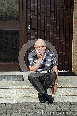 Locked out senior man sitting in front of his house Stock Photo